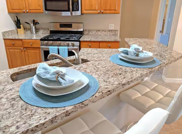 kitchen featuring brown cabinetry, appliances with stainless steel finishes, a breakfast bar area, and light stone countertops