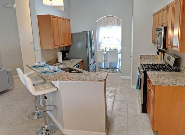 kitchen featuring a sink, stainless steel appliances, light stone countertops, and a breakfast bar area