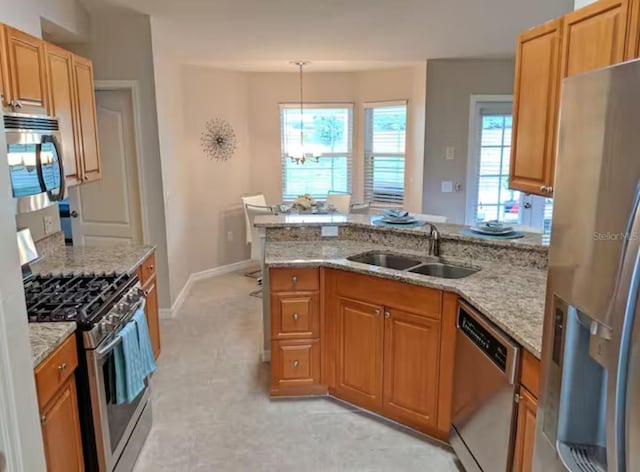 kitchen with a sink, a peninsula, light stone counters, and stainless steel appliances