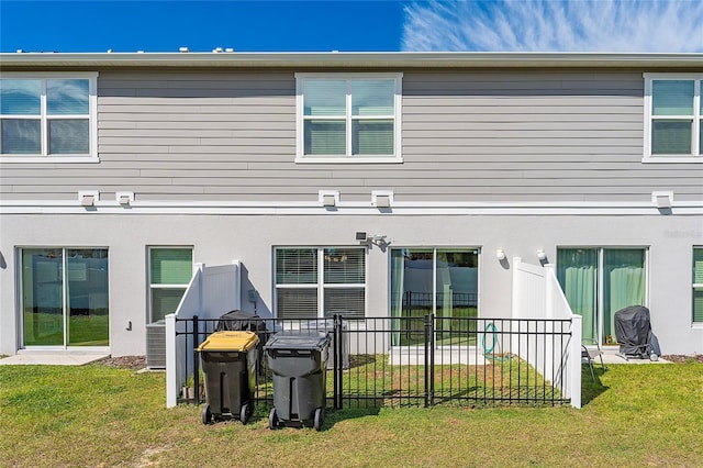 rear view of property featuring stucco siding, a lawn, and fence