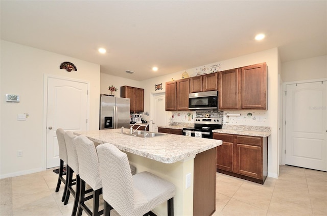 kitchen featuring a breakfast bar, a center island with sink, a sink, appliances with stainless steel finishes, and light countertops