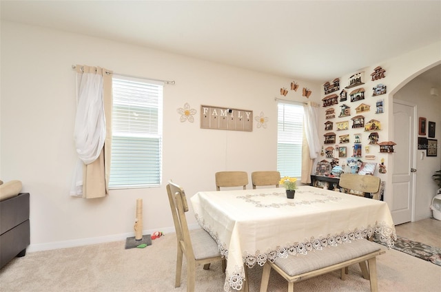 dining room featuring baseboards, arched walkways, plenty of natural light, and light carpet