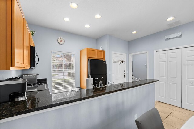 kitchen with dark stone countertops, light tile patterned floors, a peninsula, recessed lighting, and black appliances