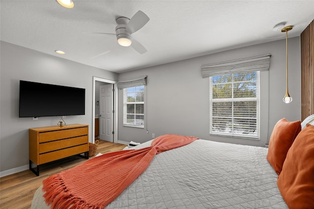 bedroom with a textured ceiling, light wood-style flooring, baseboards, and ceiling fan