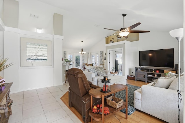 living room with light tile patterned flooring, ceiling fan with notable chandelier, high vaulted ceiling, and baseboards