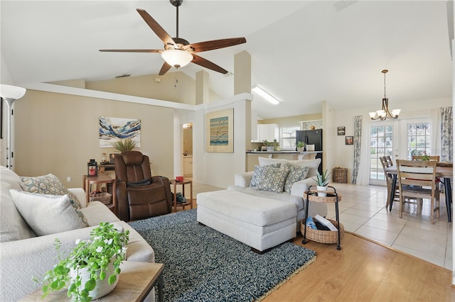 living room featuring ceiling fan with notable chandelier, light wood-style floors, and vaulted ceiling