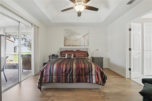 bedroom with visible vents, light wood-style flooring, a raised ceiling, and access to outside