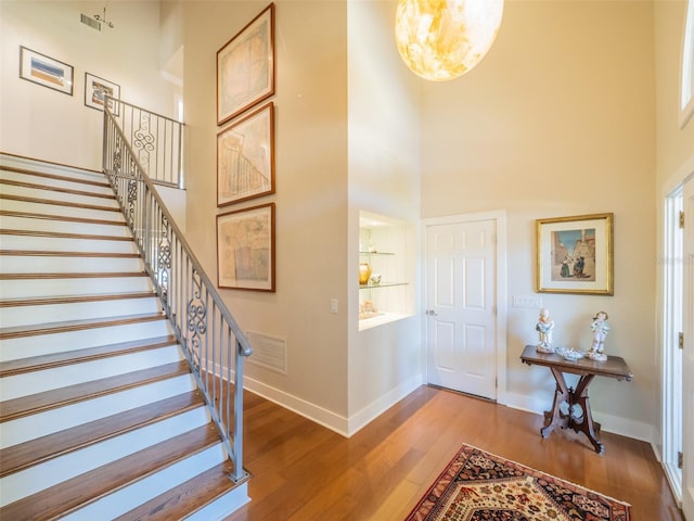 stairway with a high ceiling, wood finished floors, visible vents, and baseboards