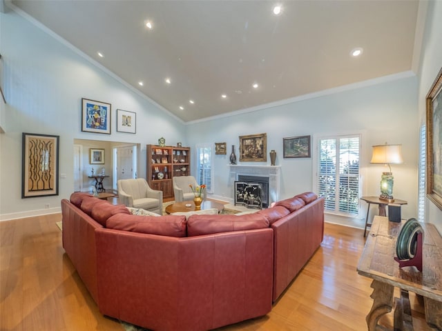 living room with a glass covered fireplace, crown molding, light wood-style floors, and high vaulted ceiling