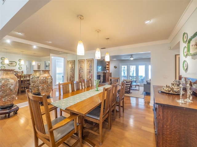 dining room featuring ceiling fan, a fireplace, light wood finished floors, and ornamental molding