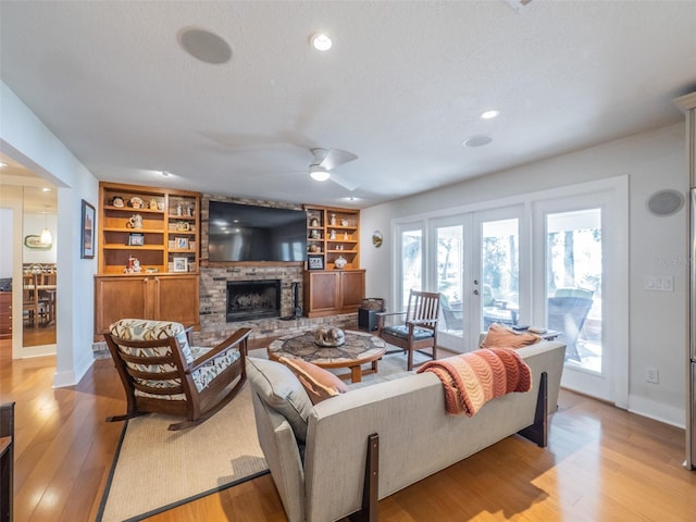 living room with a fireplace with raised hearth, ceiling fan, light wood-style flooring, french doors, and a textured ceiling