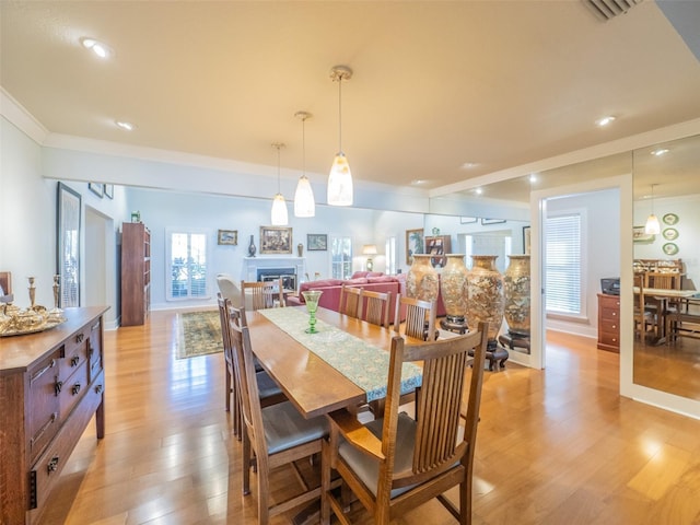 dining room featuring visible vents, a fireplace, light wood-type flooring, and ornamental molding