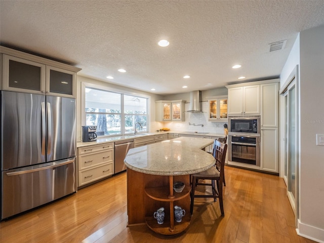 kitchen featuring visible vents, light wood finished floors, appliances with stainless steel finishes, and wall chimney range hood