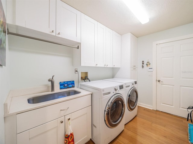 clothes washing area with a sink, a textured ceiling, cabinet space, light wood finished floors, and washing machine and clothes dryer