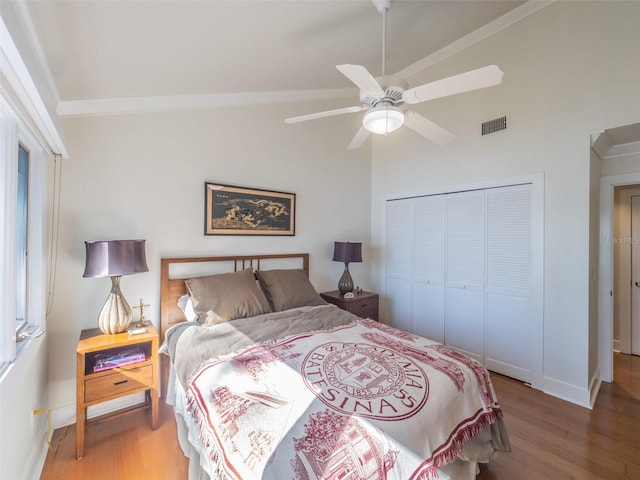 bedroom featuring wood finished floors, visible vents, lofted ceiling, a closet, and crown molding