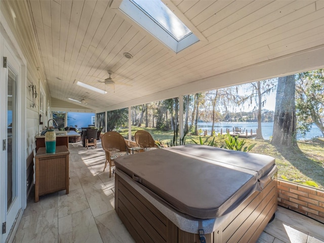 view of patio with a water view, a ceiling fan, and a hot tub