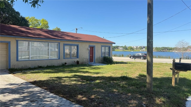 view of front facade featuring stucco siding, a front yard, and a water view