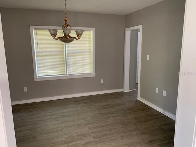 spare room with dark wood-style floors, a notable chandelier, and baseboards