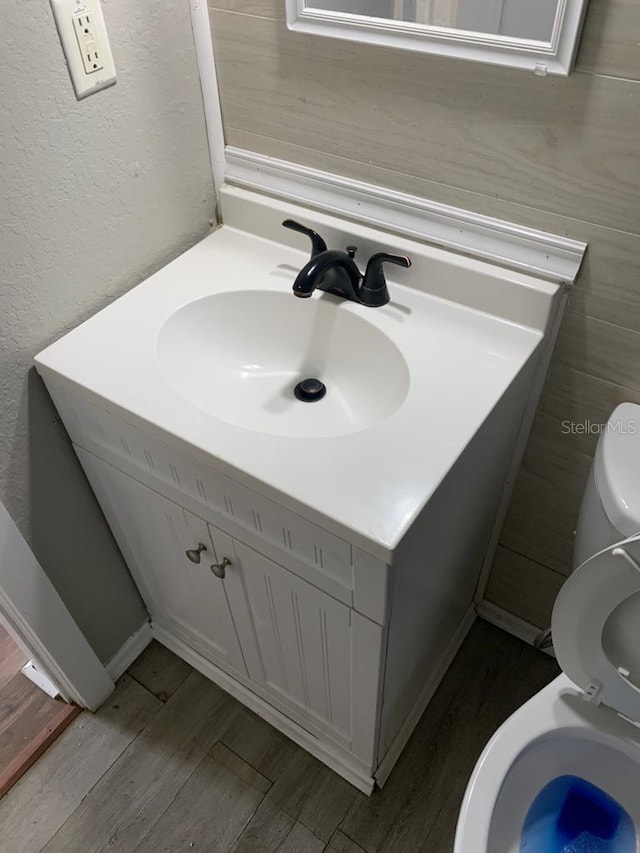 bathroom featuring toilet, vanity, a textured wall, and wood finished floors