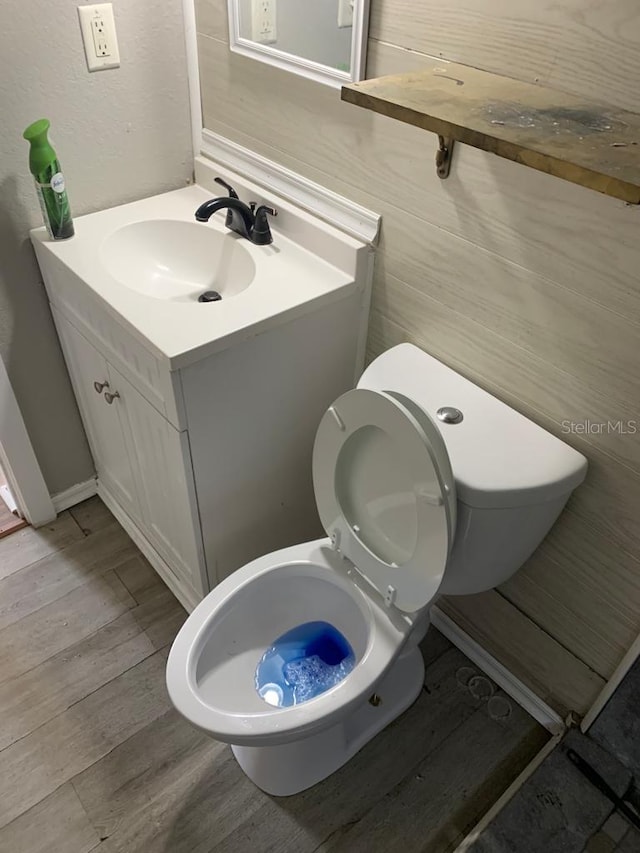 half bathroom with vanity, toilet, and wood finished floors