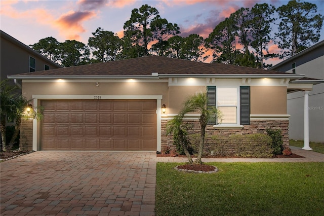 view of front facade with a yard, an attached garage, stucco siding, stone siding, and decorative driveway