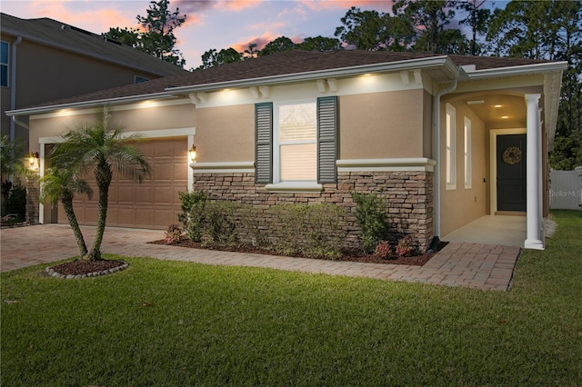 view of front of property with a front yard, an attached garage, stone siding, and stucco siding