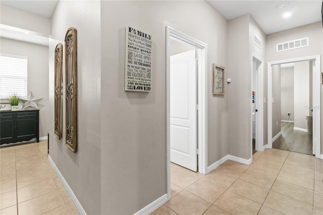 hall featuring light tile patterned flooring, visible vents, and baseboards