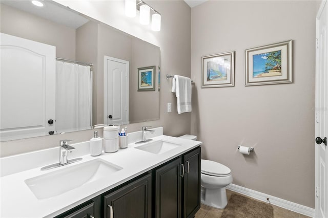 bathroom featuring double vanity, toilet, baseboards, and a sink