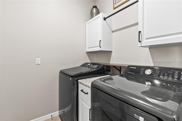 washroom featuring baseboards, cabinet space, and separate washer and dryer