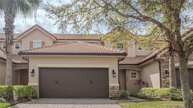 view of front of property featuring a tiled roof, stone siding, stucco siding, and an attached garage