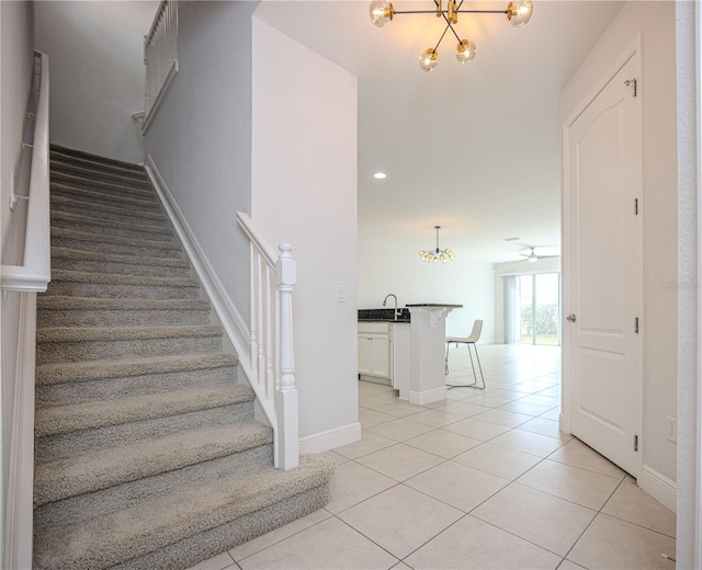 stairs featuring tile patterned floors, recessed lighting, ceiling fan with notable chandelier, and baseboards