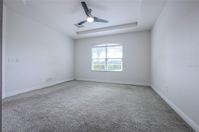 spare room with visible vents, a ceiling fan, a tray ceiling, carpet floors, and baseboards