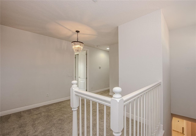 corridor featuring baseboards, carpet floors, a notable chandelier, and an upstairs landing