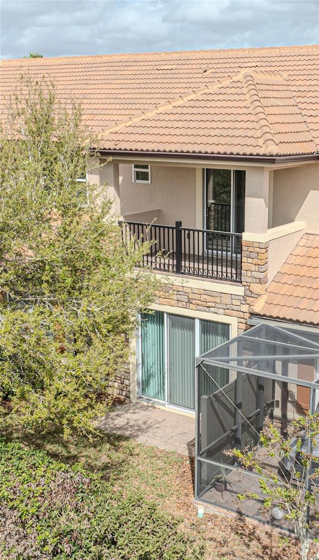 rear view of property featuring a tiled roof, glass enclosure, stucco siding, a balcony, and stone siding