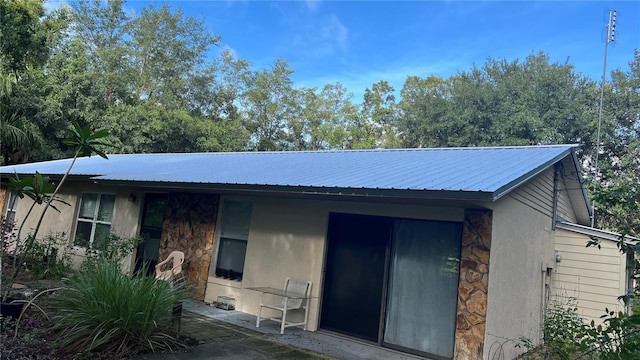 back of property with metal roof, stone siding, and a patio