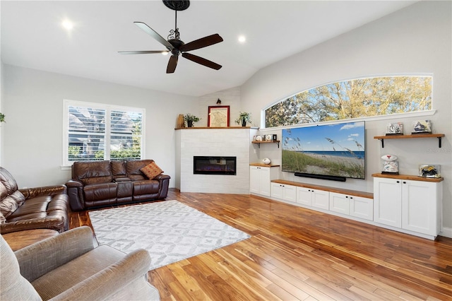 living area with recessed lighting, ceiling fan, vaulted ceiling, a tiled fireplace, and light wood-type flooring