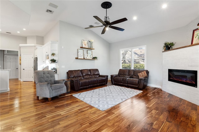 living room featuring light wood-type flooring, visible vents, a ceiling fan, a fireplace, and lofted ceiling