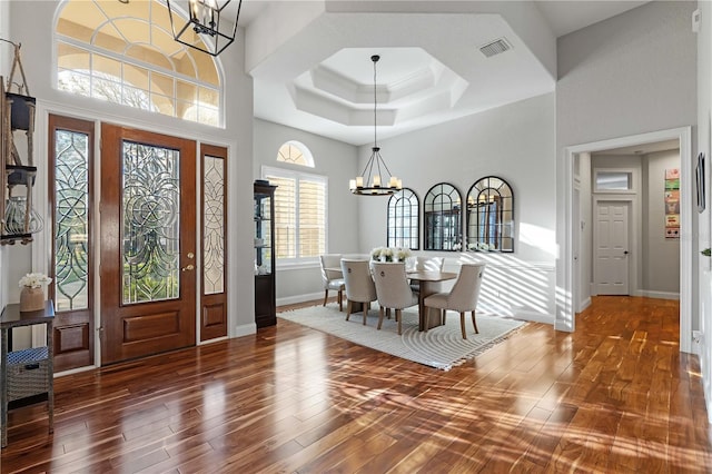 entrance foyer with visible vents, hardwood / wood-style flooring, a tray ceiling, baseboards, and a chandelier