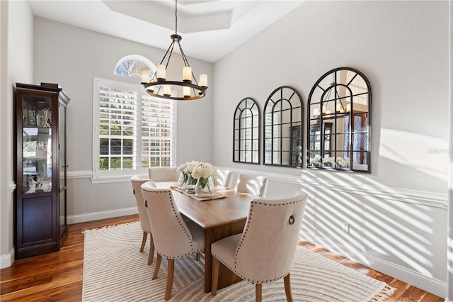 dining space with baseboards, a raised ceiling, an inviting chandelier, and wood finished floors