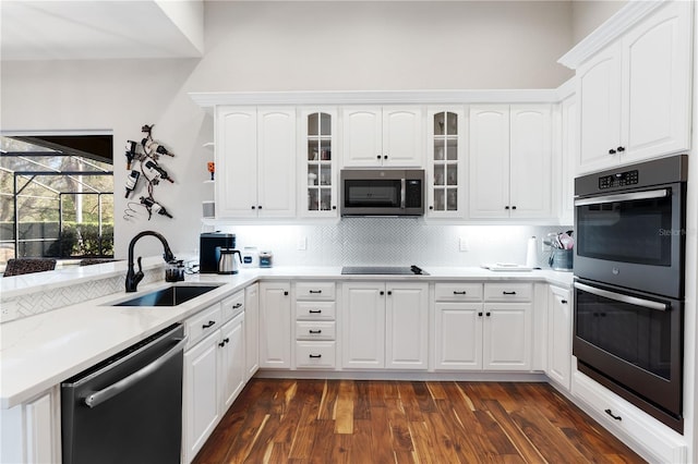 kitchen with dishwashing machine, a sink, glass insert cabinets, stainless steel microwave, and multiple ovens