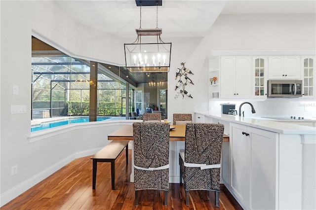 kitchen with decorative backsplash, stainless steel microwave, dark wood finished floors, white cabinets, and glass insert cabinets