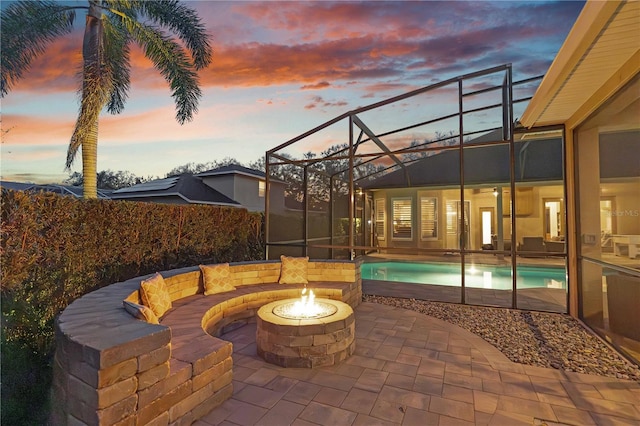 patio terrace at dusk with a lanai, a fenced in pool, and a fire pit