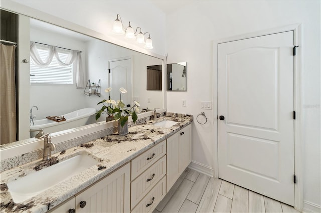 bathroom with double vanity, a freestanding tub, baseboards, and a sink