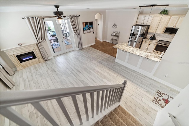 interior space featuring arched walkways, decorative backsplash, light wood-style floors, appliances with stainless steel finishes, and crown molding