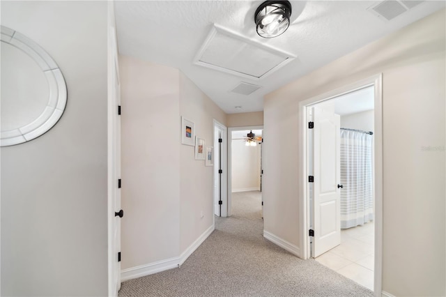 corridor with visible vents, light carpet, baseboards, and attic access