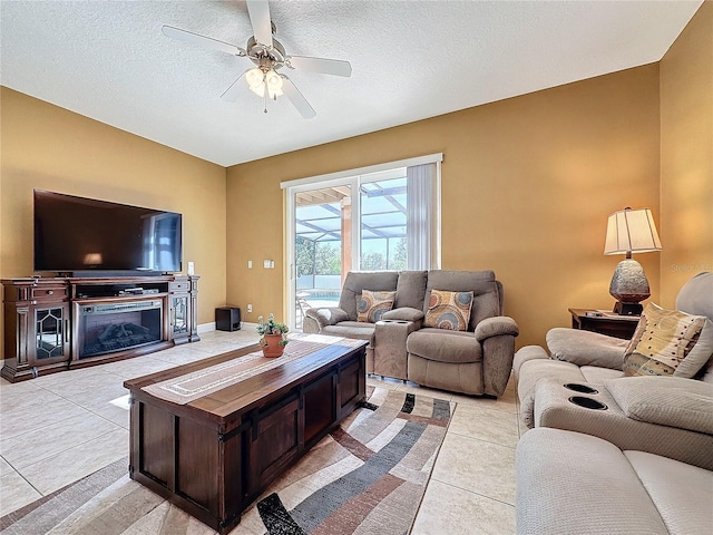 living area with a glass covered fireplace, a textured ceiling, ceiling fan, and light tile patterned flooring