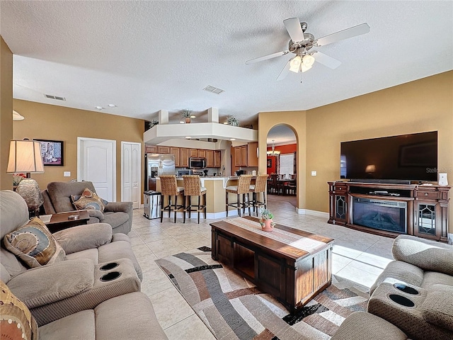 living room featuring visible vents, light tile patterned flooring, arched walkways, a textured ceiling, and ceiling fan with notable chandelier