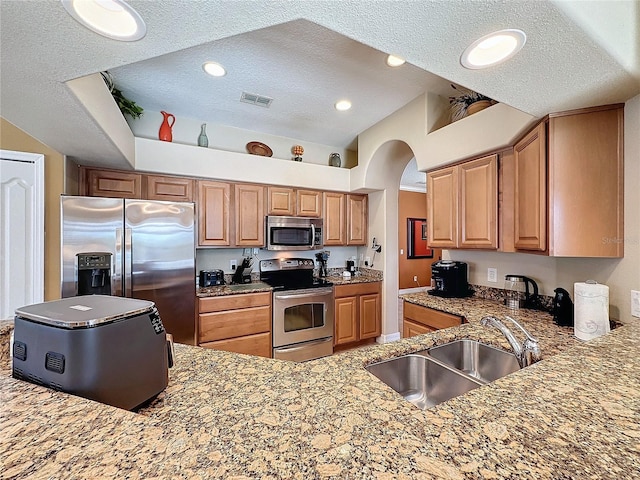 kitchen with visible vents, light stone countertops, appliances with stainless steel finishes, a textured ceiling, and a sink