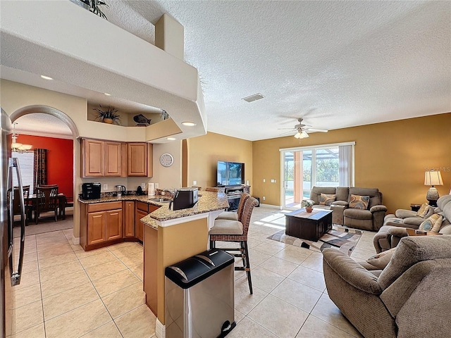 kitchen with open floor plan, light tile patterned floors, light stone counters, a kitchen breakfast bar, and a peninsula