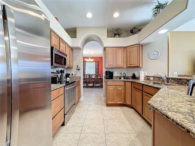 kitchen with dark stone countertops, light tile patterned flooring, arched walkways, a sink, and appliances with stainless steel finishes